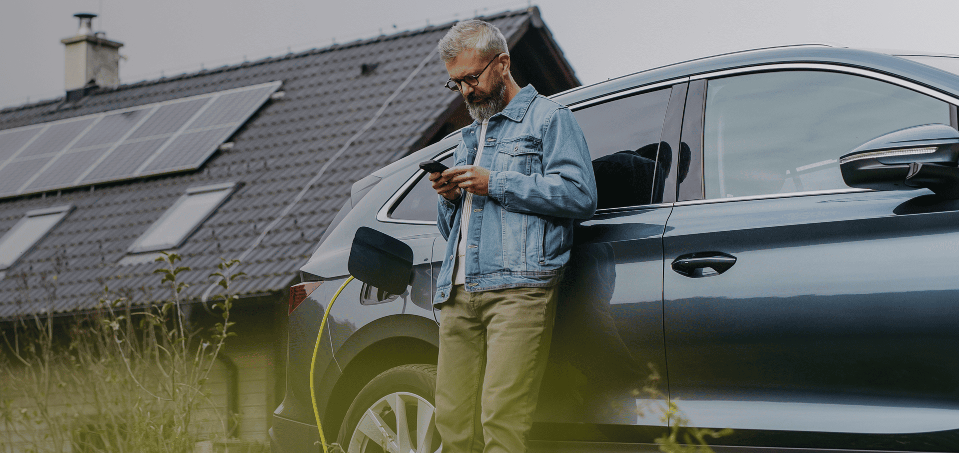 Haus mit Photovoltaikanlage, Person lädt entspannt sein E-Auto